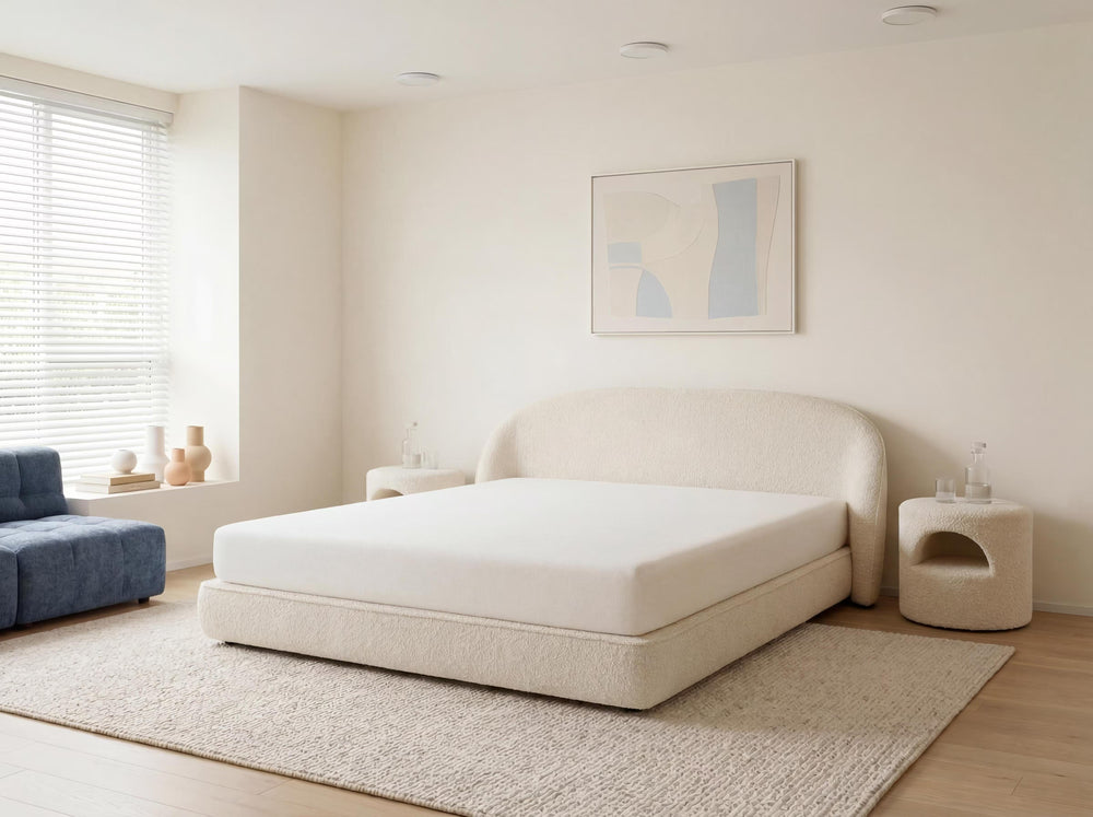 Beige bed in a minimalistic bedroom with light wood flooring and white walls.