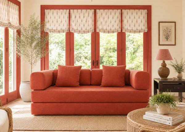 Living room with a red sofa, wicker chair, and large windows.